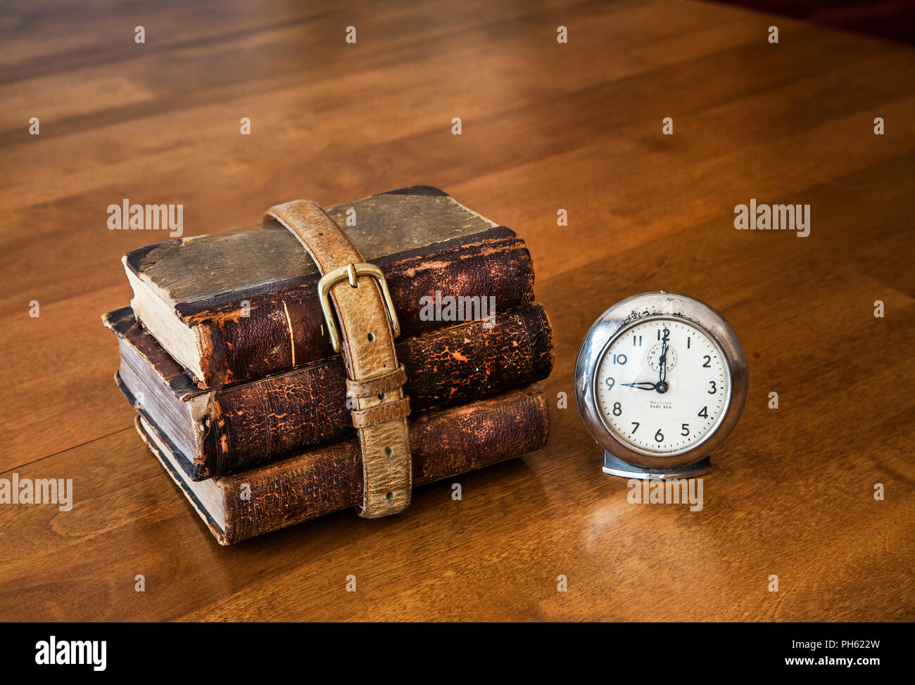 Three school books rapped with a old belt on a desk with a vintage clock, still life, USA, school books desk historical images American Stock Photo