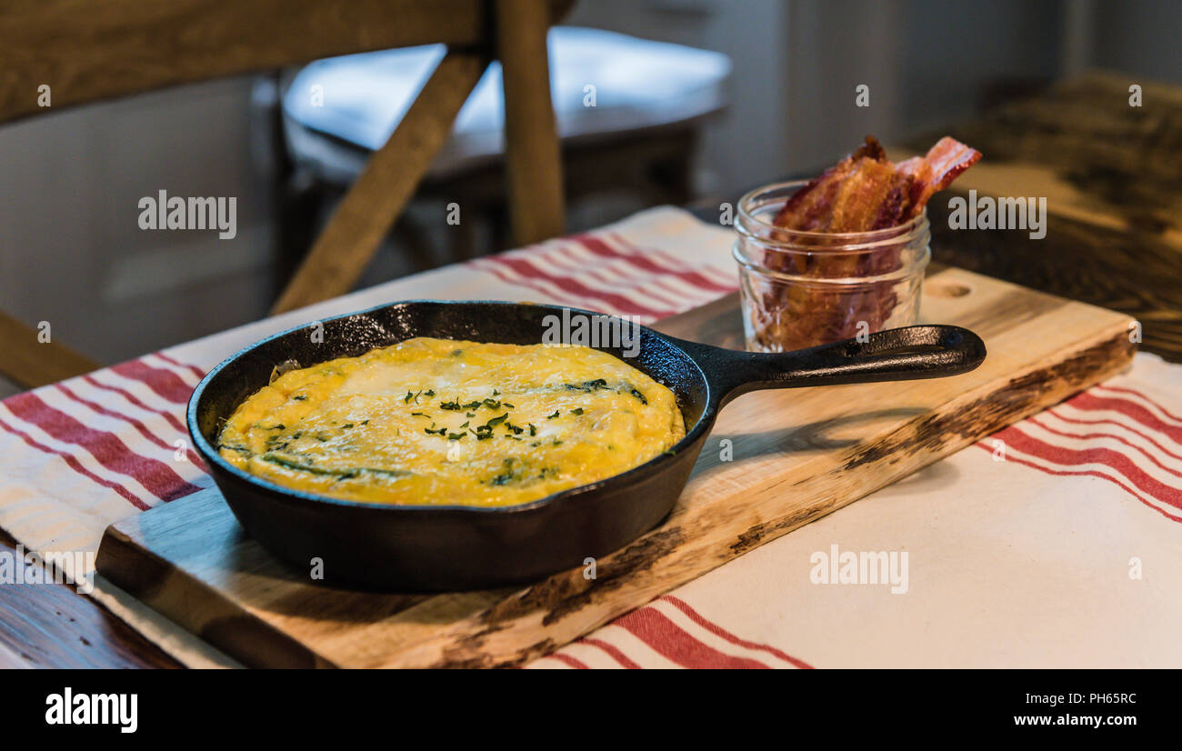 Savory omelette presented in iron skillet and bacon served upright in mason jar. Stock Photo