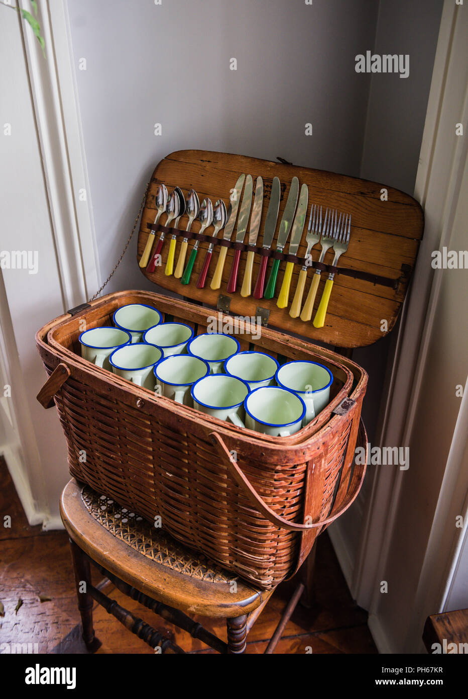 Open retro wicker picnic basket filled with white cups and silverware. Stock Photo