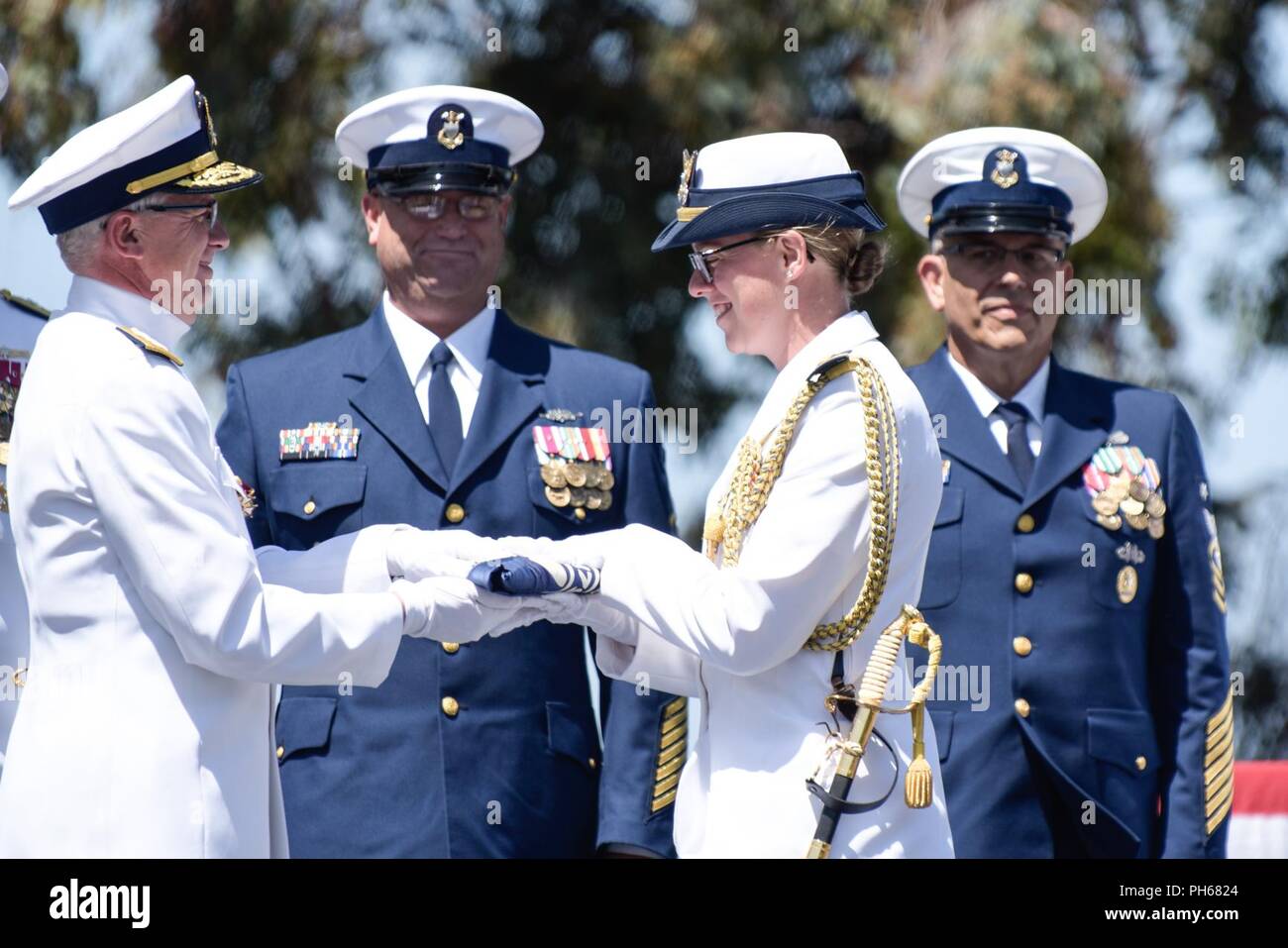 Rear Admiral Todd Sokalzuk, the Coast Guard’s 11th District commander, hands his personal flag to his aide, Lt. Julia Kane, during his change-of-command ceremony at Coast Guard Island in Alameda, California, June 28, 2018, as the active-duty and reserve command master chiefs look on. During the ceremony, Rear Admiral Peter Gautier replaced Sokalzuk as the district commander as Sokalzuk heads to the east coast to be the deputy commander of Coast Guard Atlantic Area. Stock Photo
