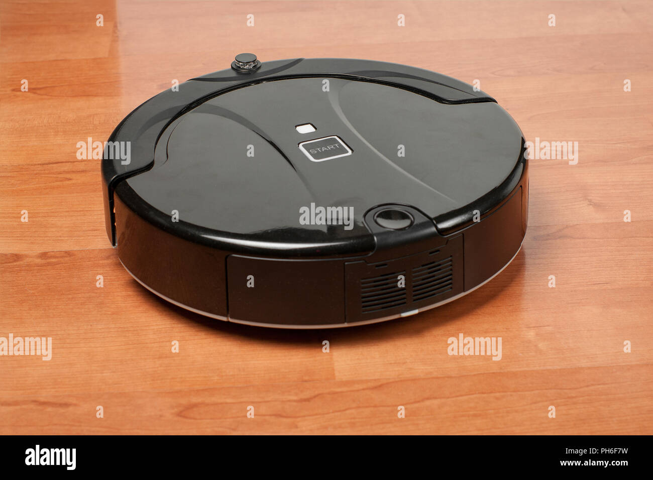 black robotic vacuum cleaner runs on the laminate floor. The robot is