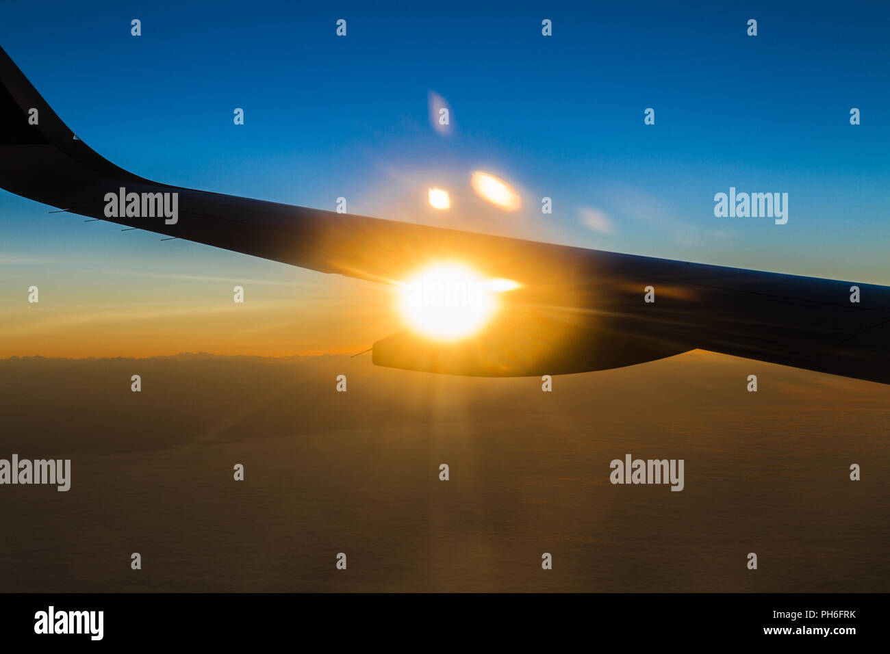 Panoramic aerial view of a colourful flaring tropical sunset trough an airplane window. Stock Photo