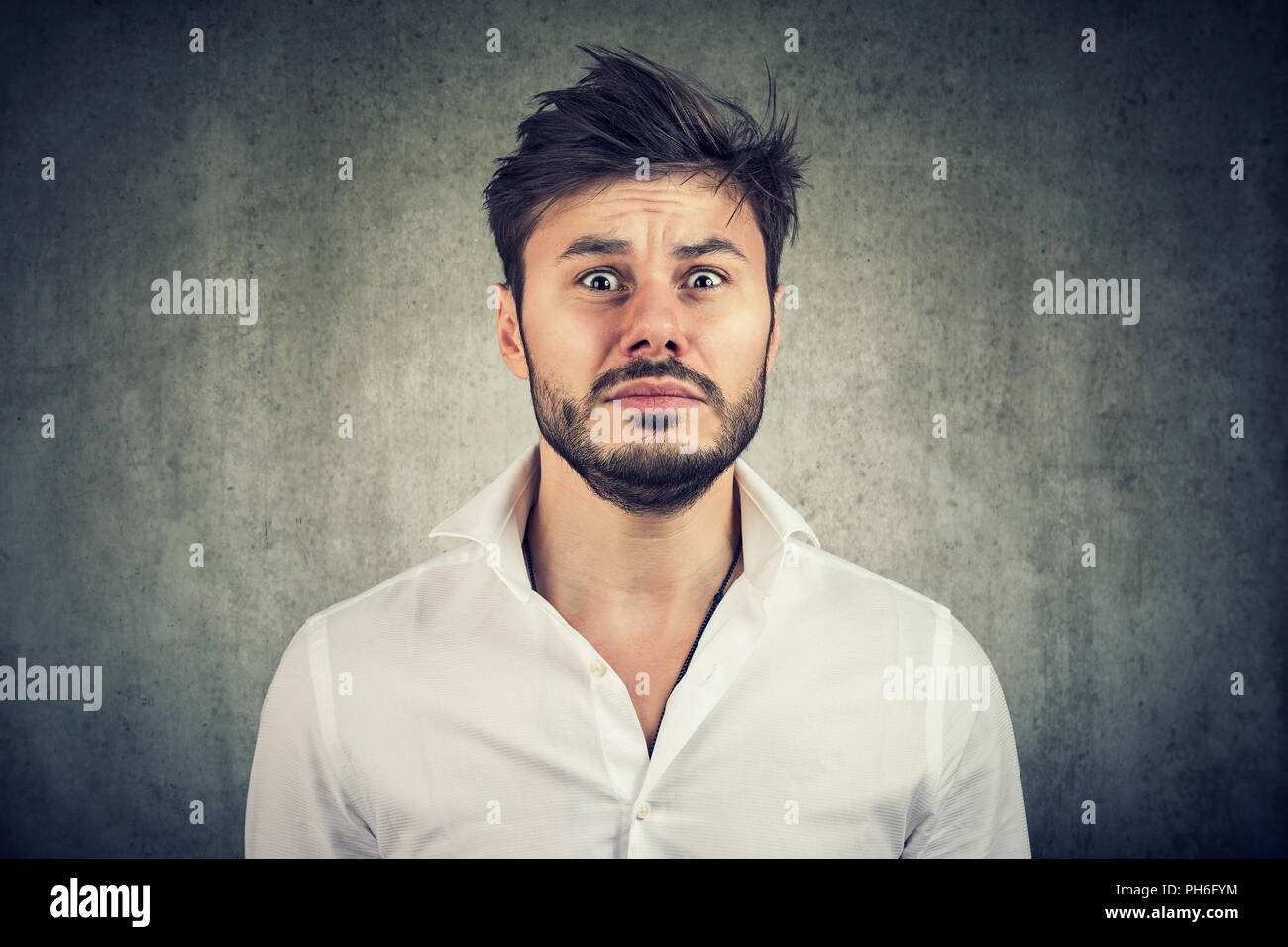 Adult bearded man looking at camera in fear being in panic on gray background Stock Photo