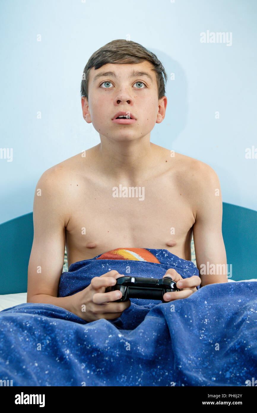 Teenage boy playing a video game while sitting up in bed Stock Photo