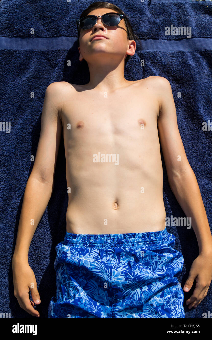 Caucasian teenage boy sunbathing in a garden wearing sunglasses