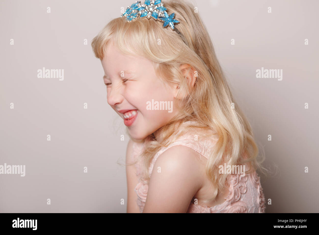 Closeup portrait of cute adorable white blonde fair Caucasian preschool girl in pink dress and princess crown. Child smiling laughing posing in studio Stock Photo