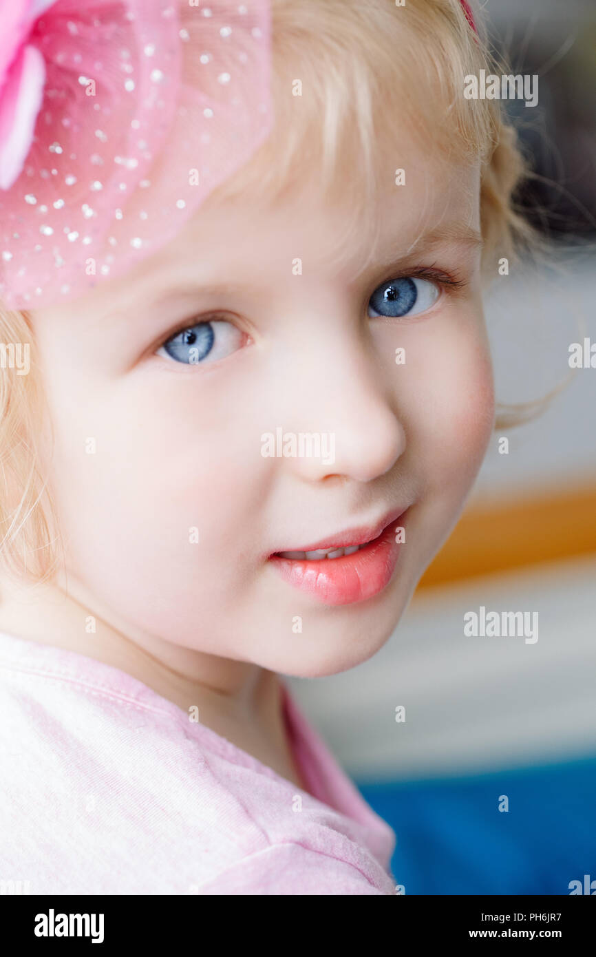 Closeup portrait of cute adorable blonde white Caucasian smiling baby girl with large blue eyes wearing pink headband, looking in camera Stock Photo