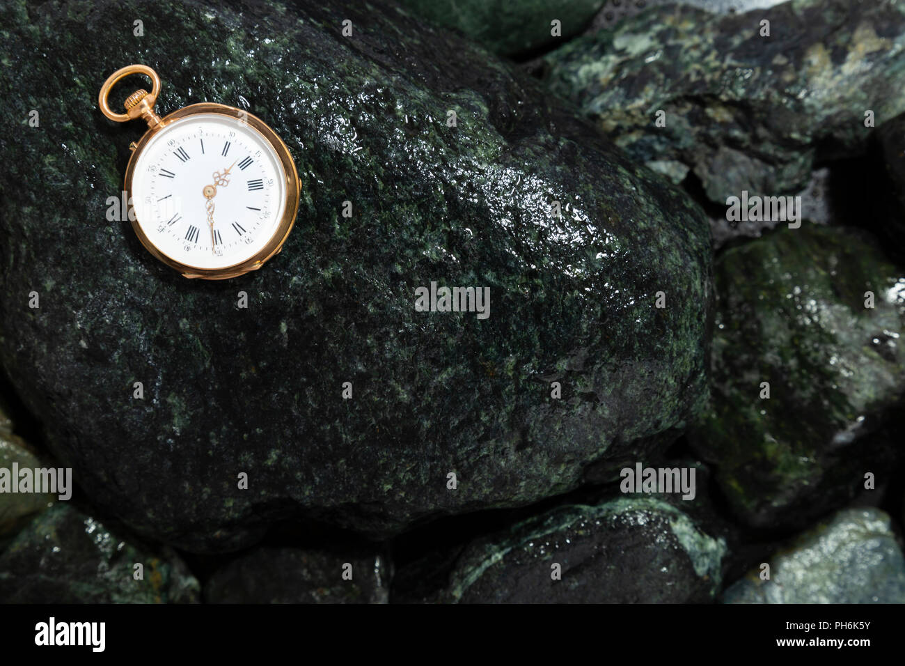 Closeup of a beautiful classic gold pocket watch laying on wet green stones Stock Photo