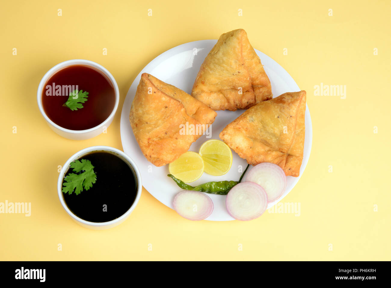 Punjabi Veg Samosa with onion and lemon slices with green chili and chutney on wooden background, samosa is a popular street food in India Stock Photo