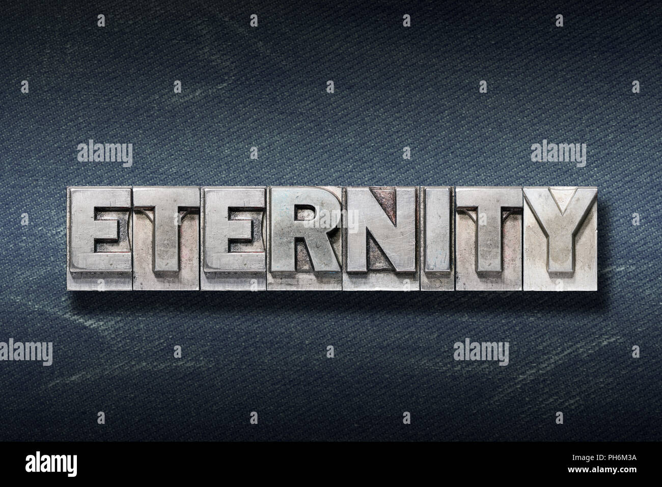 eternity word made from metallic letterpress on dark jeans background Stock Photo