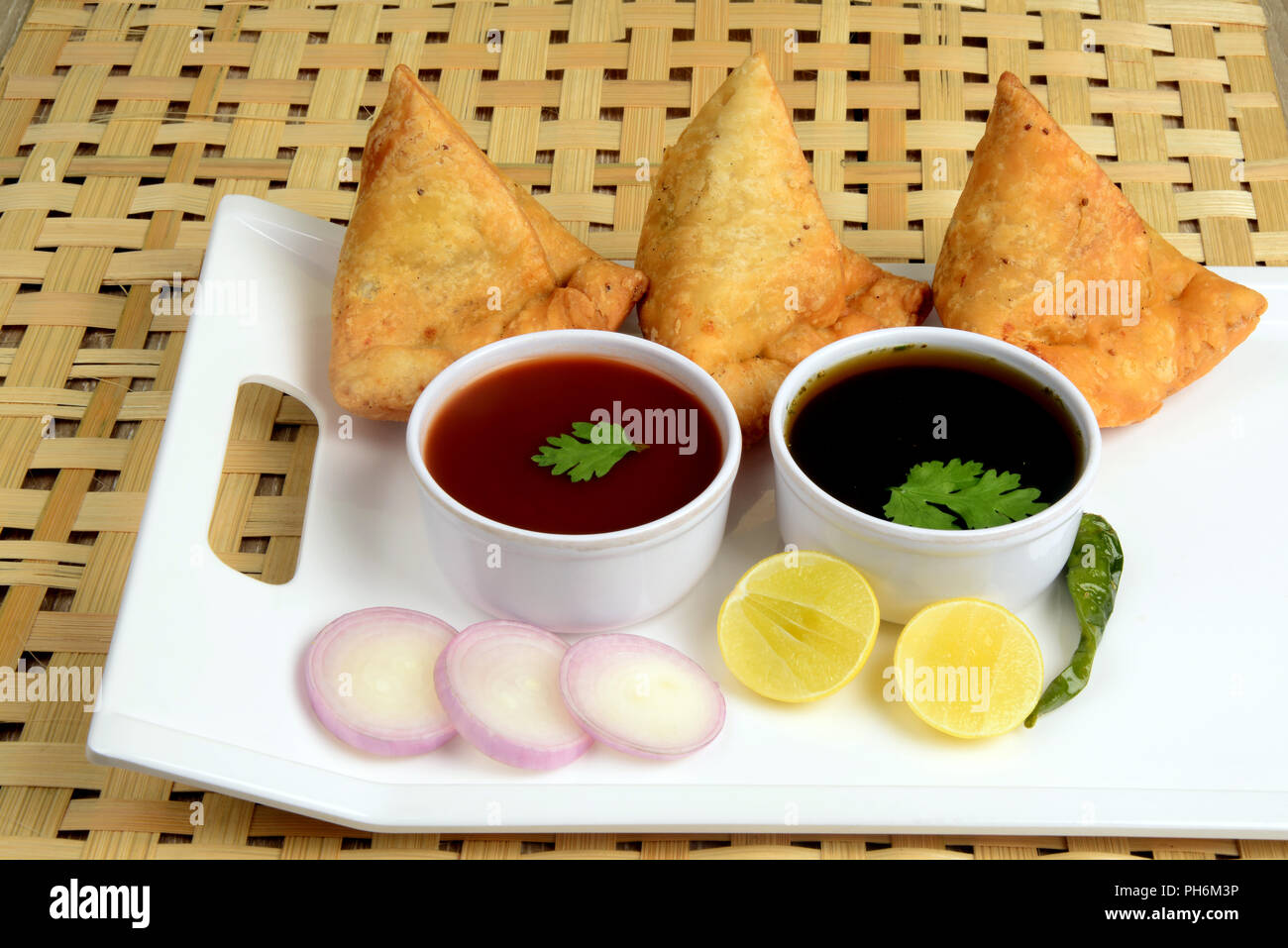 Punjabi Veg Samosa with onion and lemon slices with green chili and chutney on wooden background, samosa is a popular street food in India Stock Photo