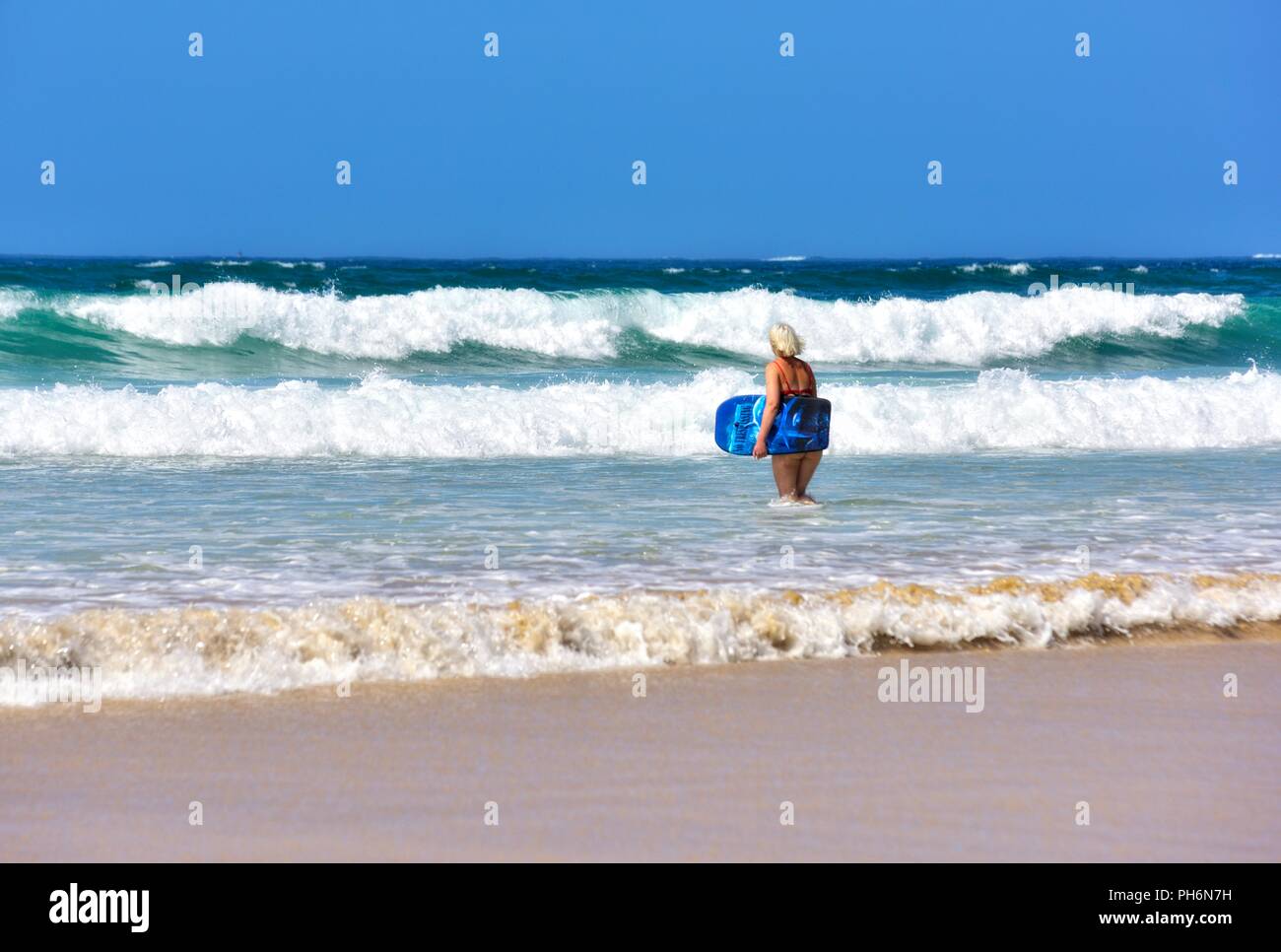 Blond woman walking into the sea with a body board,Riviere Towans beach