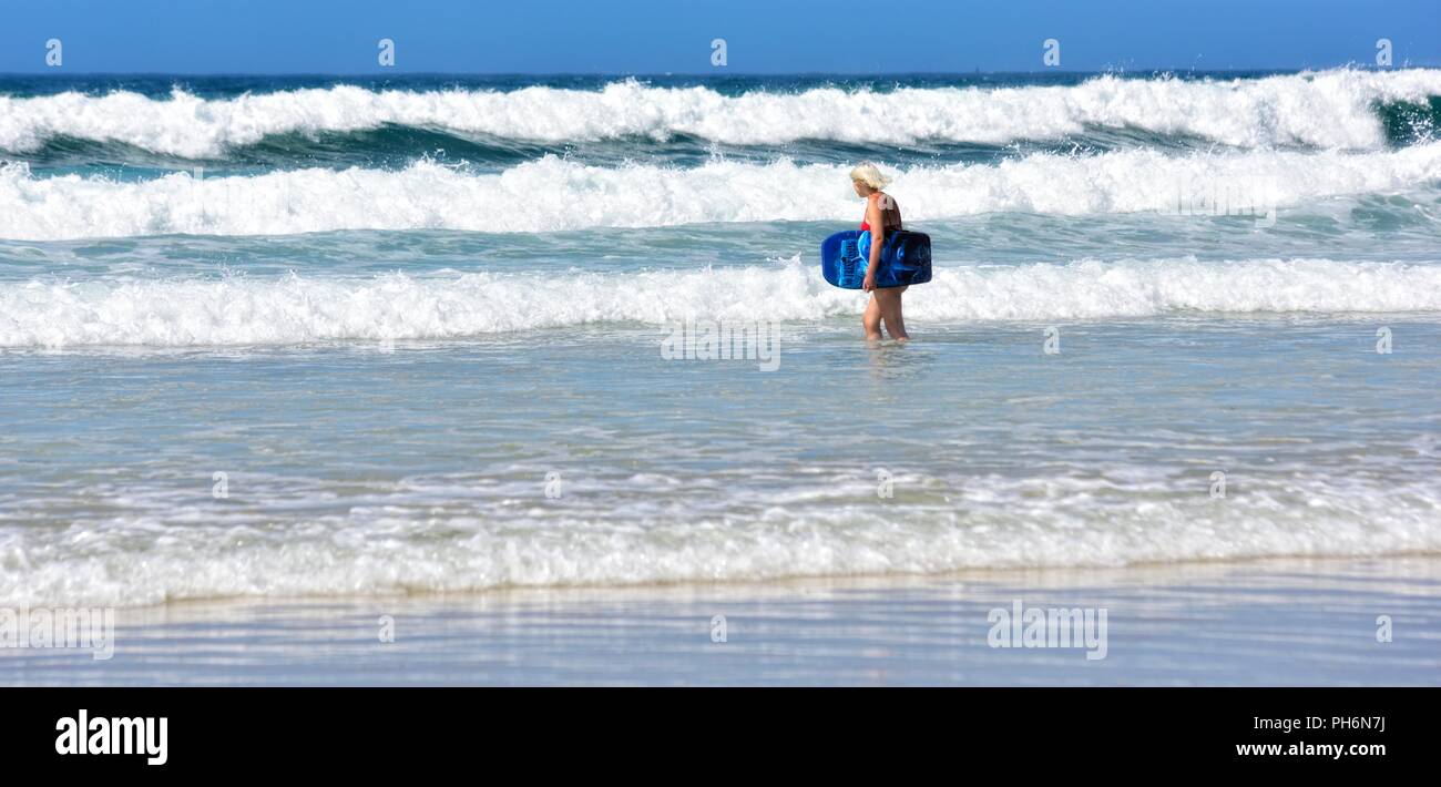 Blond woman walking into the sea with a body board,Riviere Towans beach