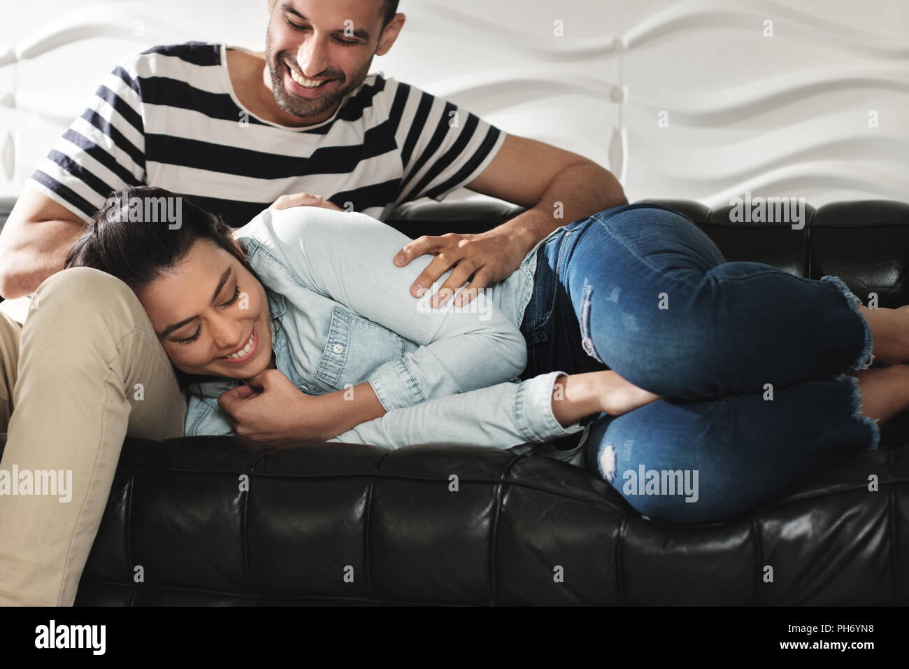 Happy Latino Couple Having Fun And Laughing On Sofa Stock Photo