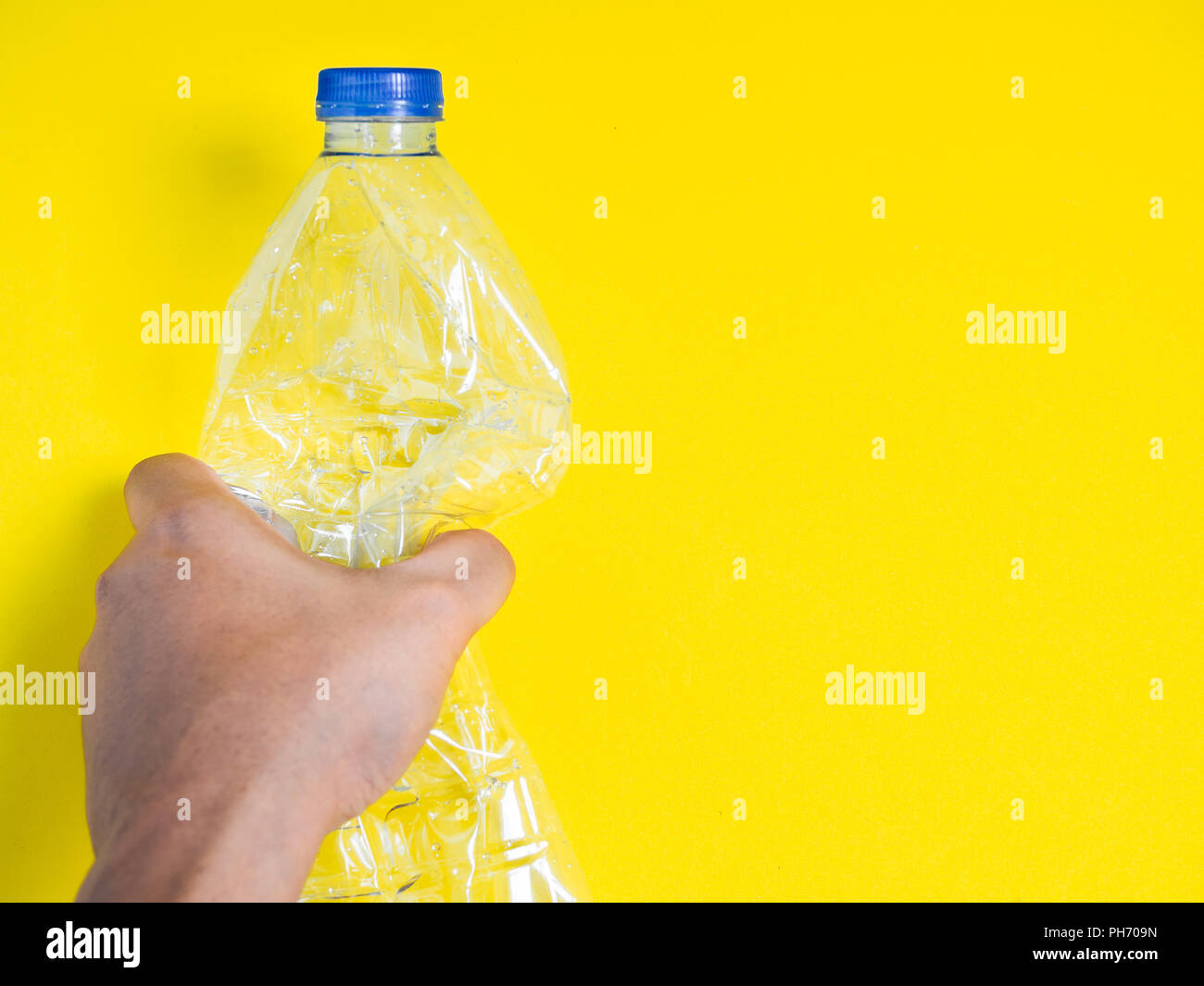 Hand squeezing recycle clear plastic drink water bottle on yellow