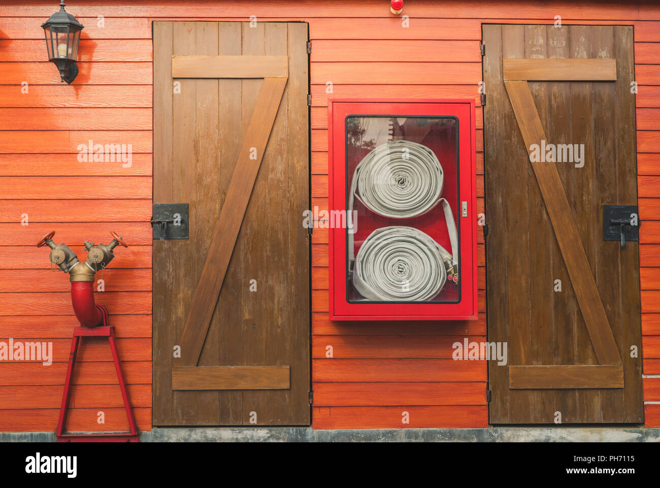 Fire hose in red cabinet hanging on orange wooden wall. Fire emergency equipment box for safety and security system. Fire safety pump. Deluge system o Stock Photo