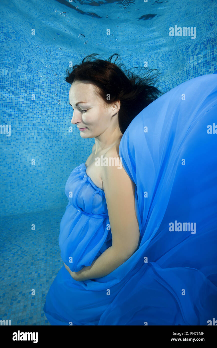 Pregnant woman in a blue dress posing underwater in the pool Stock Photo