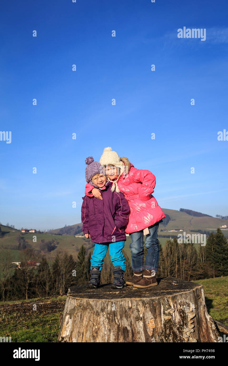 Two girls standing on a trunk in hilly landscape Stock Photo