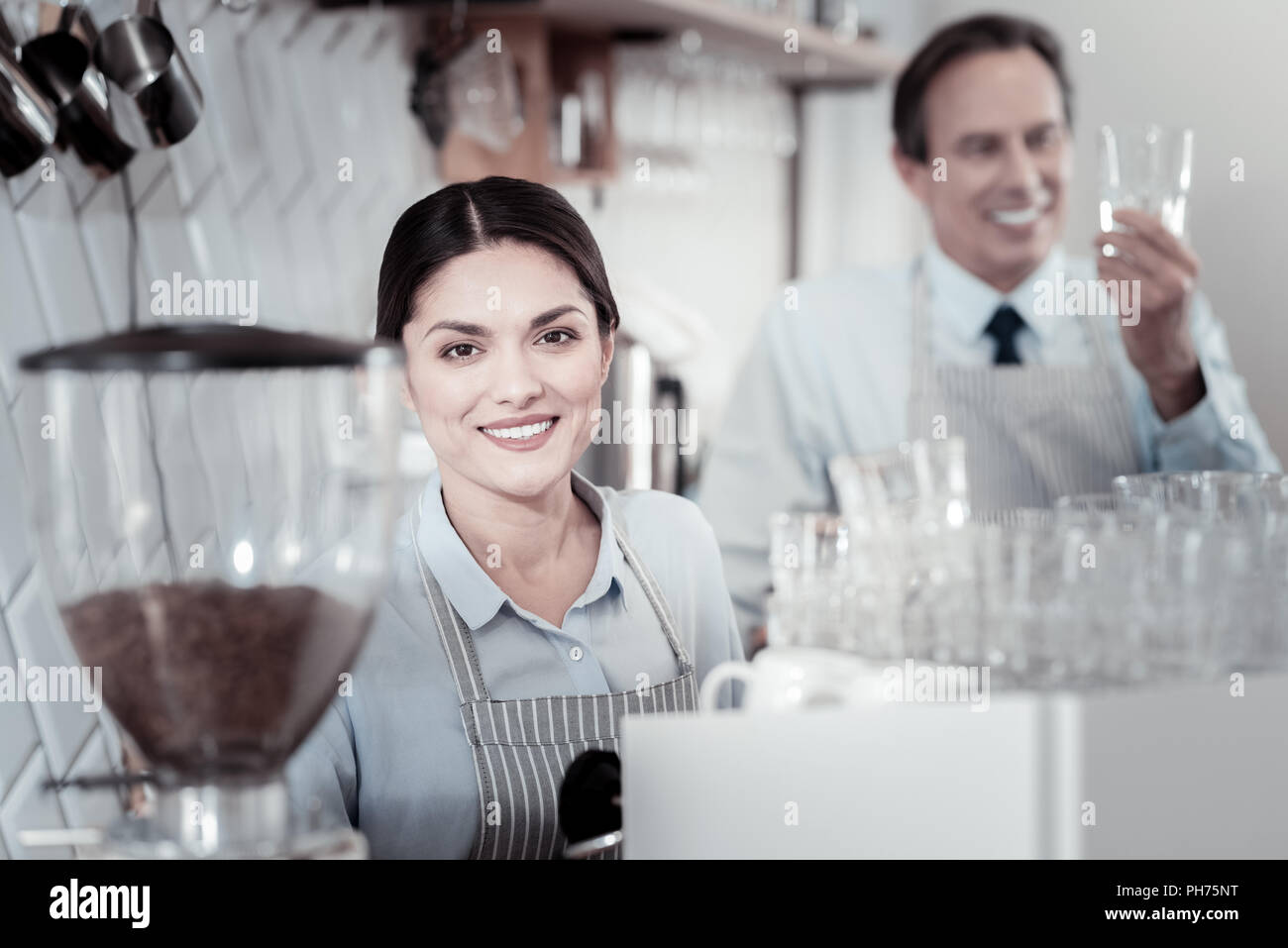 Pretty waitress smiling while standing near the coffee machine Stock Photo