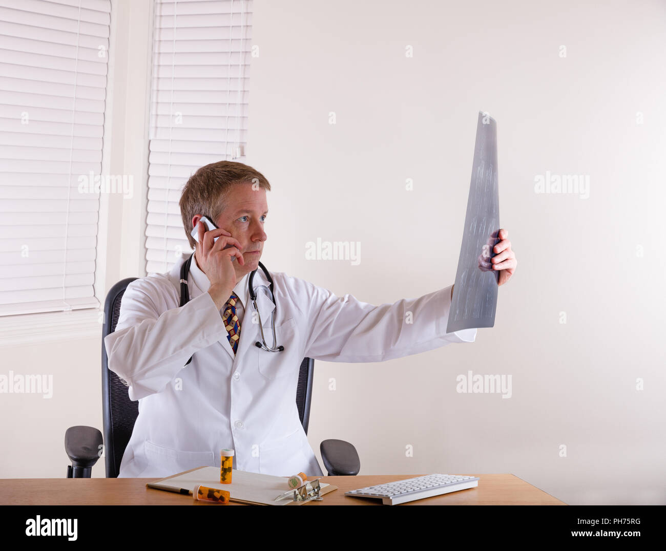 Doctor looking over x-ray chart while communicating on cell phone Stock Photo