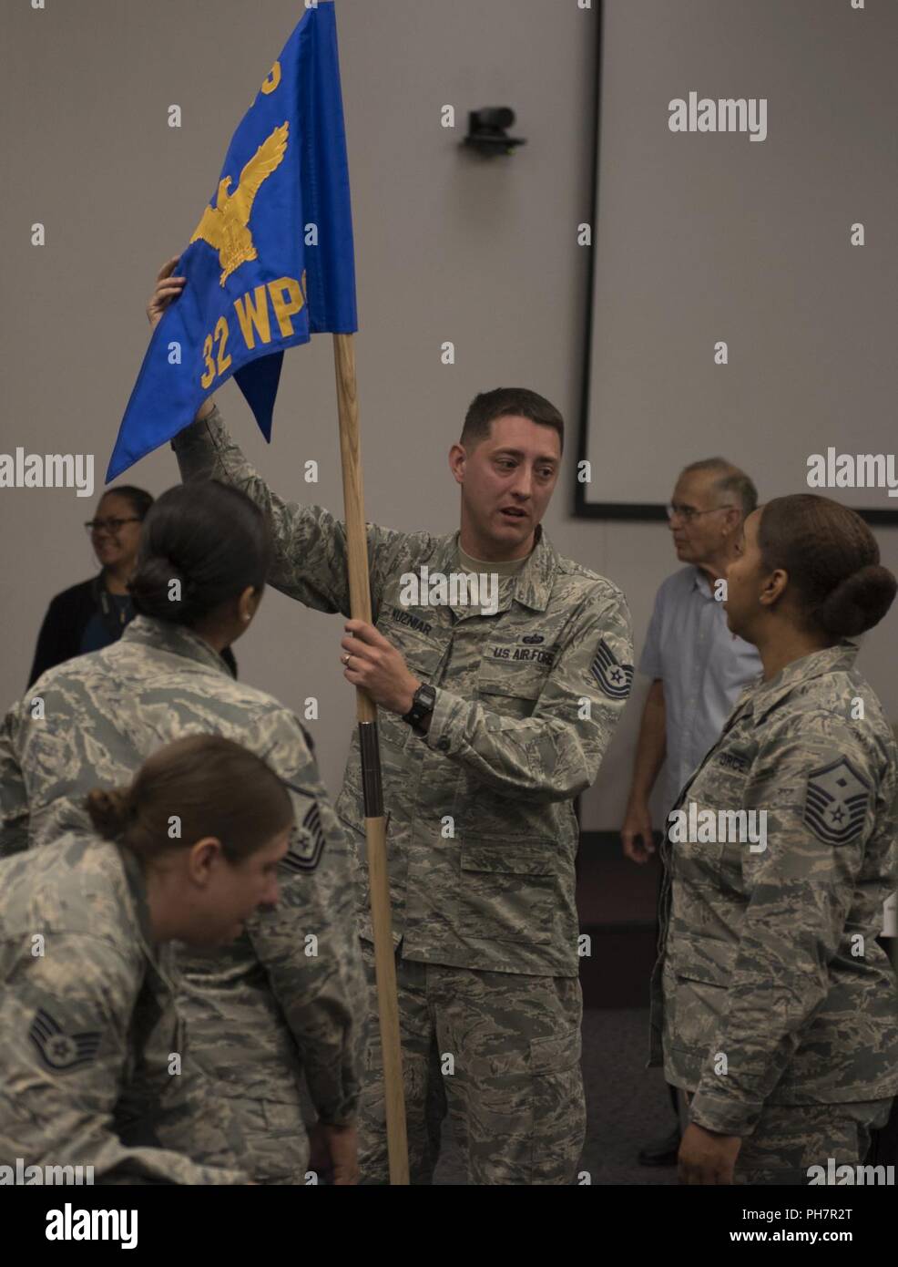 Tech. Sgt. Kieth Kuzniar, 32nd Weapons Squadron superintendent, shows off the new squadron guidon to Master Sgt. Brandi Love, U.S. Air Force Weapons School first sergeant, during an assumption of command ceremony at Nellis Air Force Base, Nevada, June 28, 2018. The 32nd WPS will focus on teaching Cyber Warfare Operations. Stock Photo