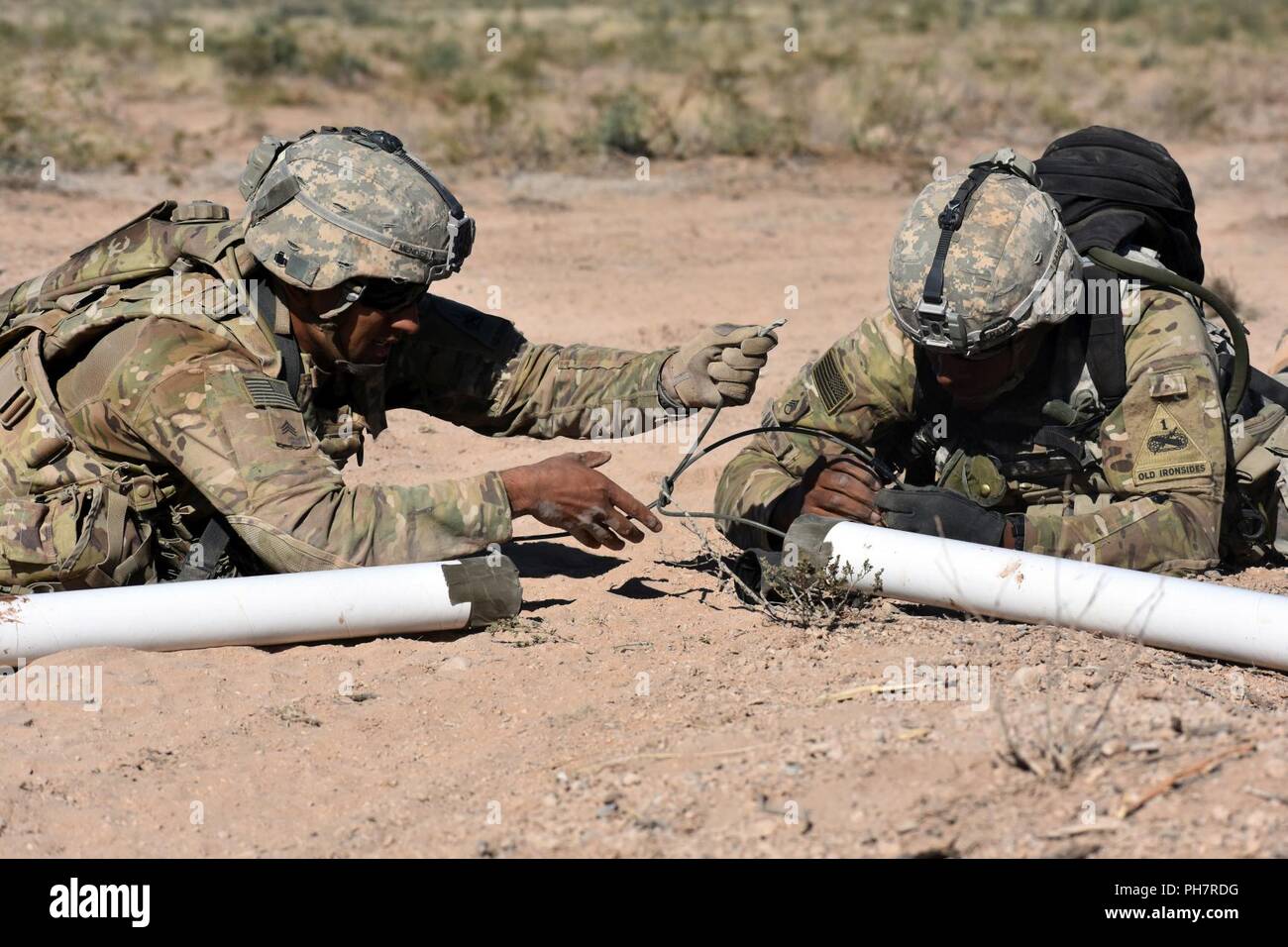 Sgt. Luis Mendez, left, and Staff Sgt. Barjona Ray, assigned to the 16th Brigade Engineer Battalion, 1st Stryker Brigade Combat Team, 1st Armored Division, assist Company C, 4th Battalion, 17th Infantry Regiment, by setting up a simulated Bangalore Torpedo charge as Soldiers practice breaching through an obstacle at the Malakhand training village, Orogrande Range Complex, N.M., June 24, 2018. Stock Photo
