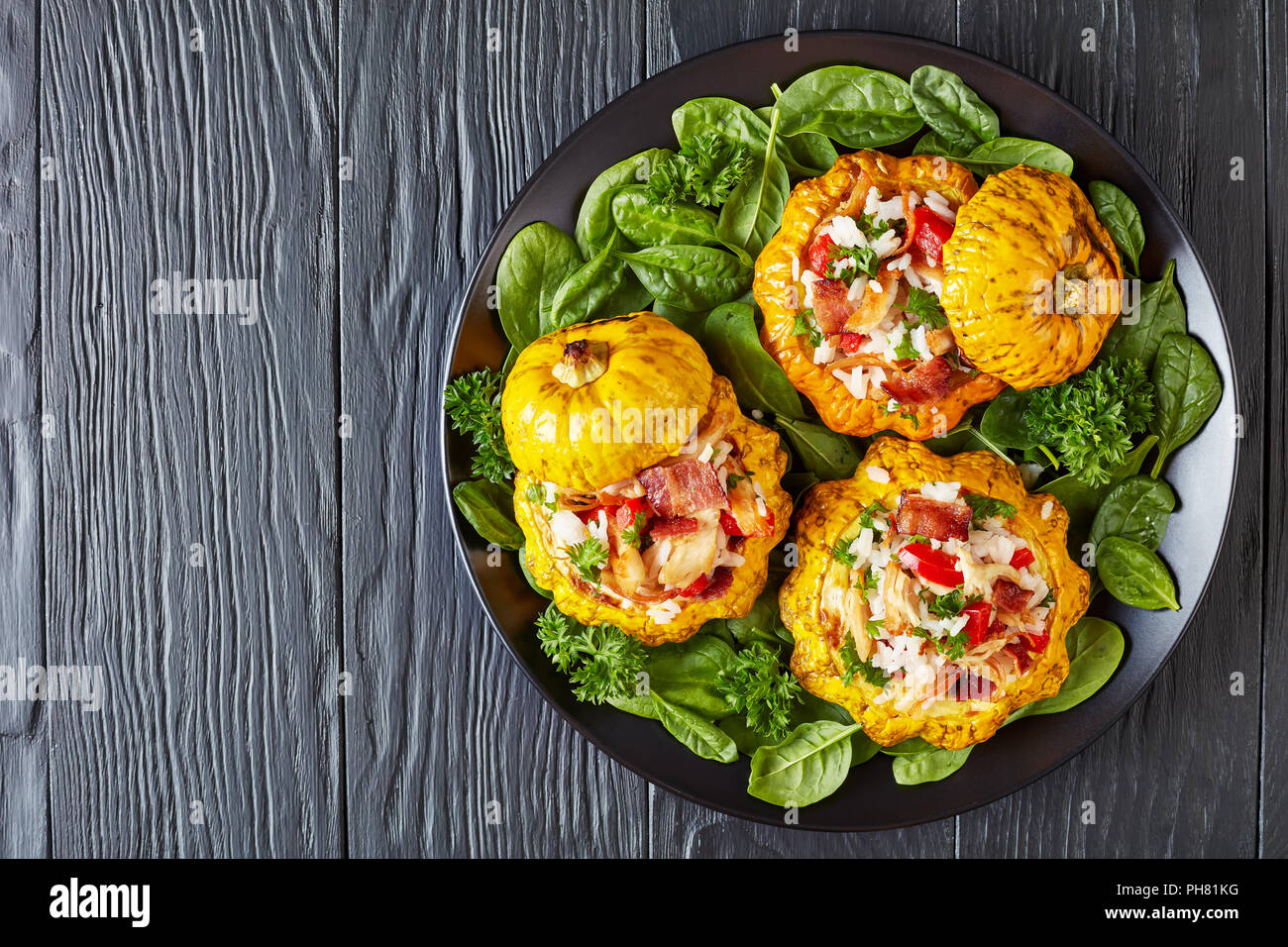 baked Patty Pan squash stuffed with rice, fried chicken meat, crispy fried bacon, bell pepper and served with green fresh spinach leaves and parsley o Stock Photo