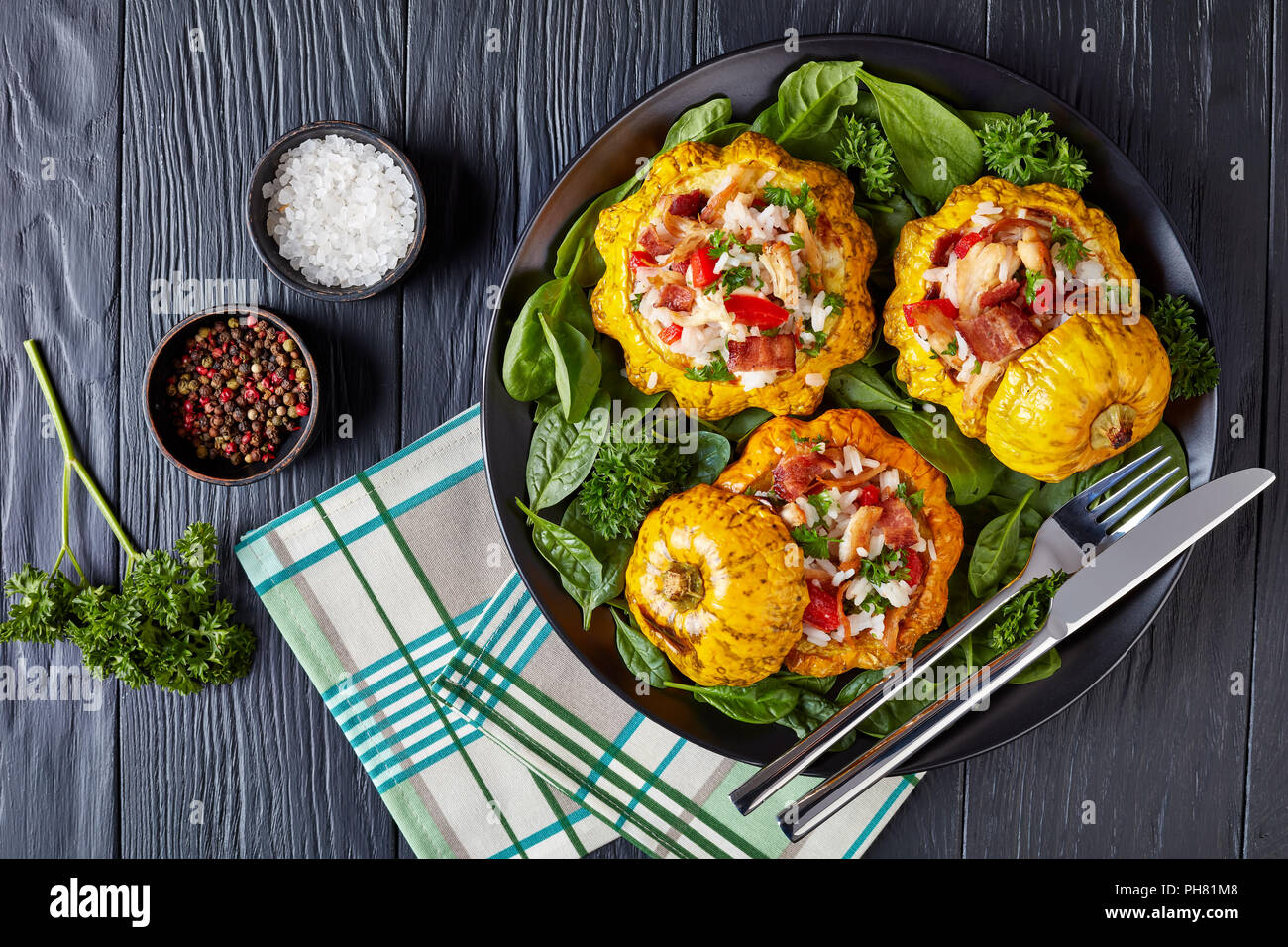 close-up of baked Pattypan squash stuffed with rice, fried chicken meat, crispy fried bacon, red bell pepper and served with spinach leaves and parsl Stock Photo