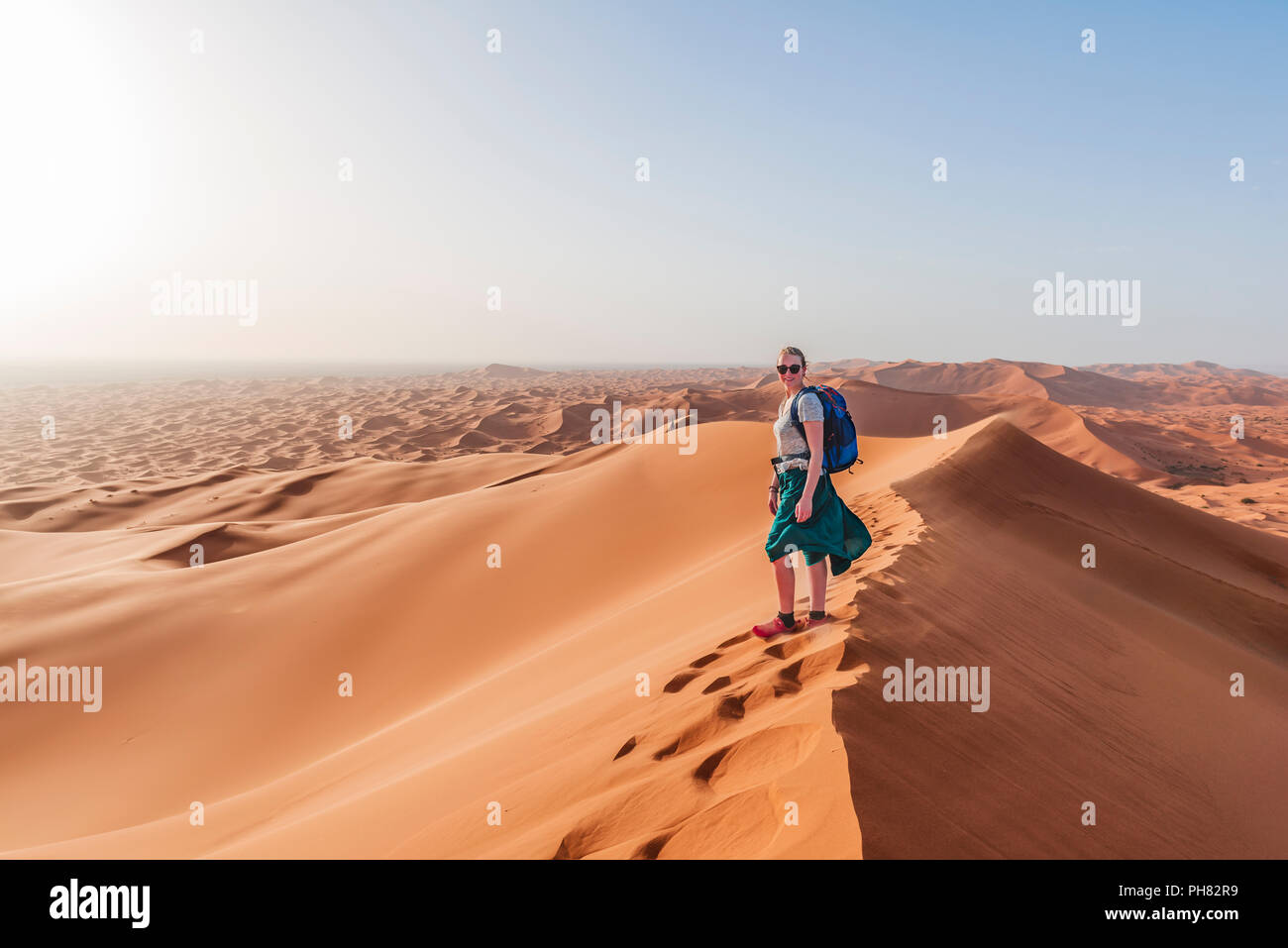 Female hiker on a red sand dune in the desert, dune landscape Erg Chebbi, Merzouga, Sahara, Morocco Stock Photo