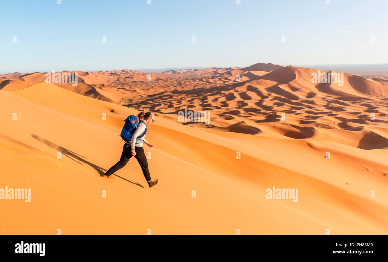Woman running downhill, red sand dunes in the desert, dune landscape Erg Chebbi, Merzouga, Sahara, Morocco Stock Photo