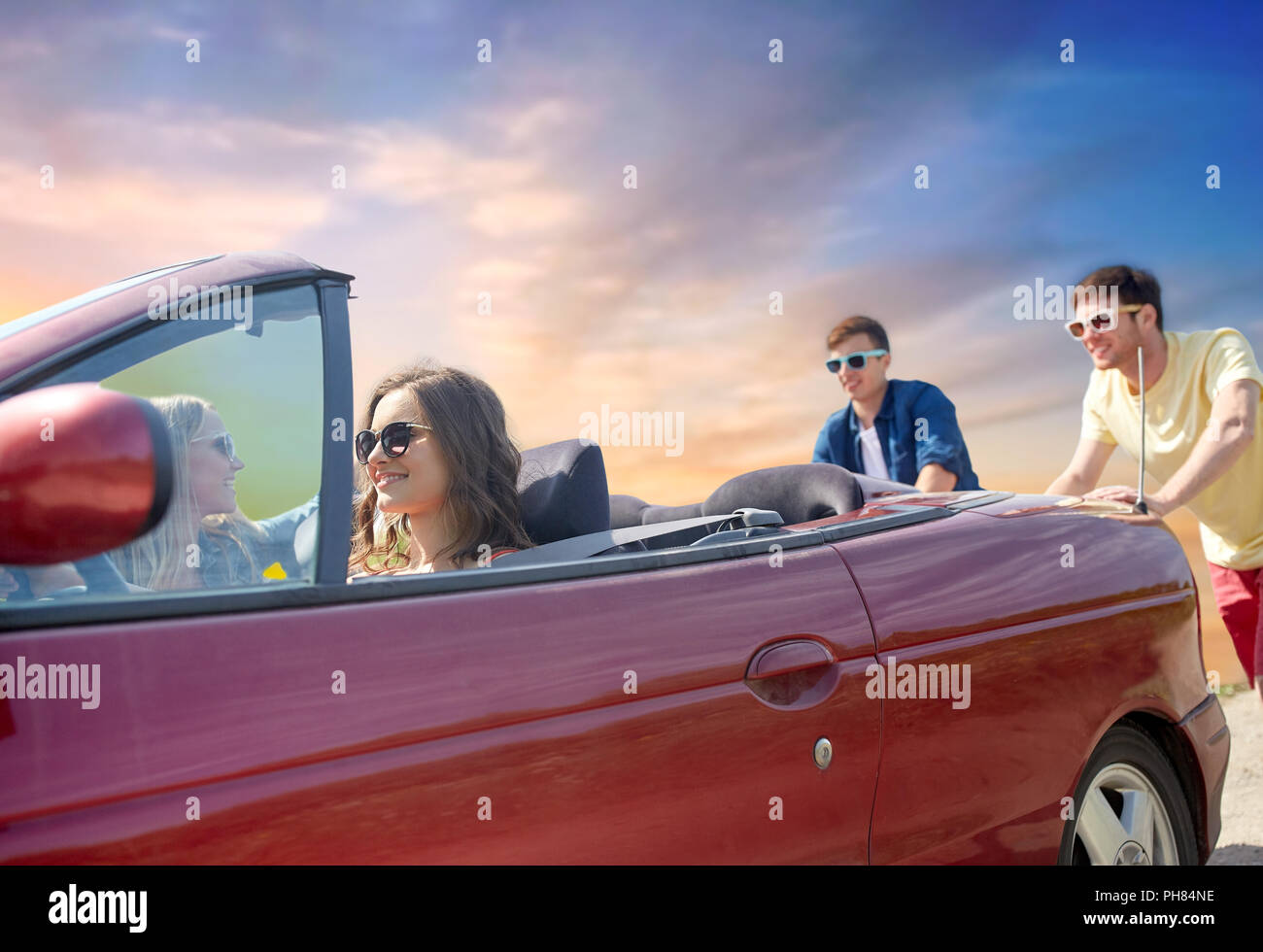 friends pushing broken convertible car Stock Photo