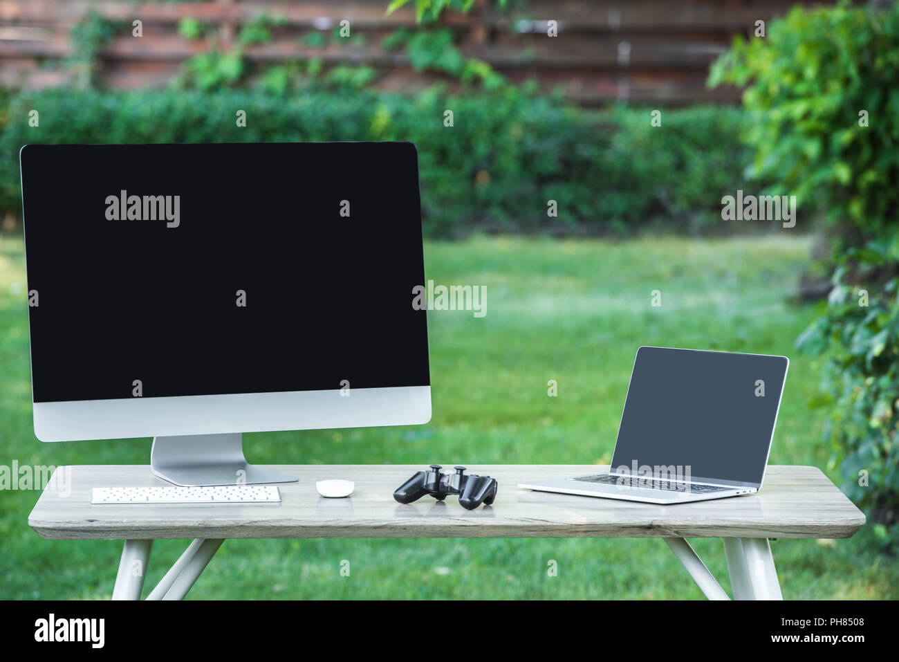 selective focus of joystick, computer and laptop with blank screens on table outdoors Stock Photo