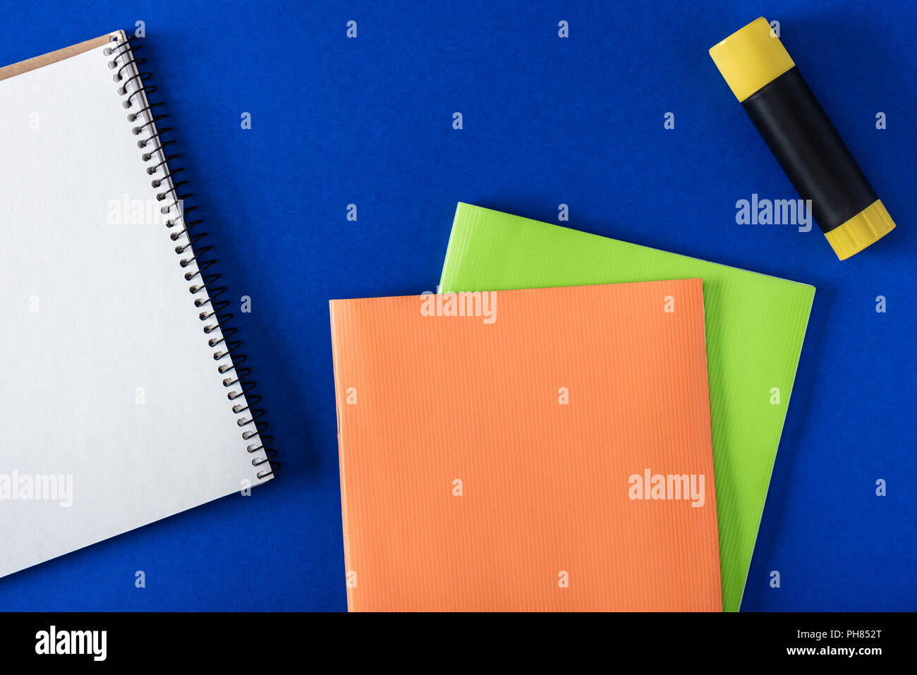 top view of blank notebook, glue stick and textbooks on blue background