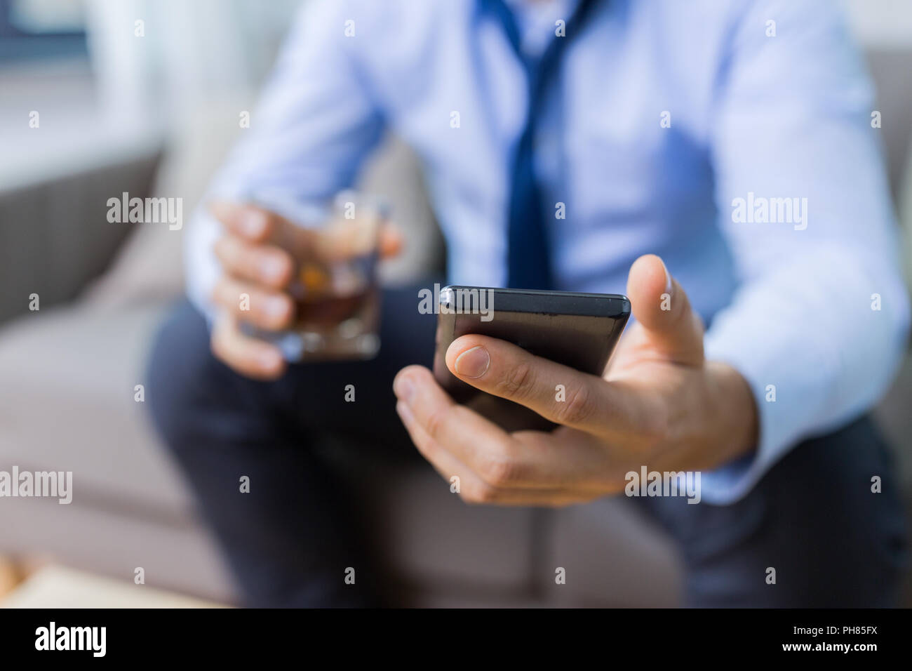 man with smartphone and glass of alcohol at home Stock Photo