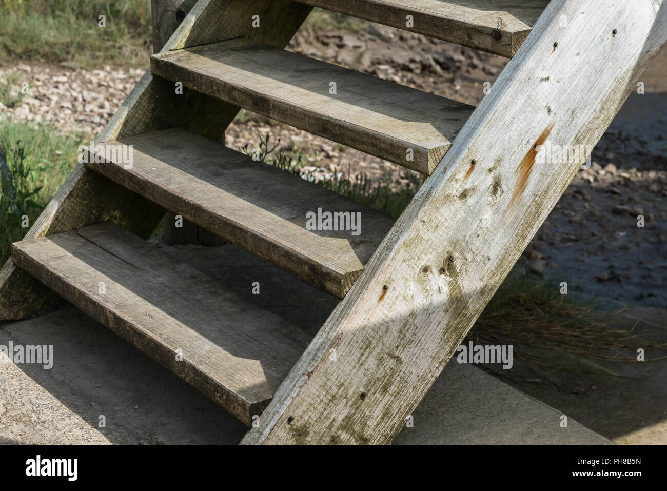 Homemade wooden access steps in close up with sun and shadows going up to a jetty at the riverside at Skippool Creek in Lancashire, England, UK. Stock Photo