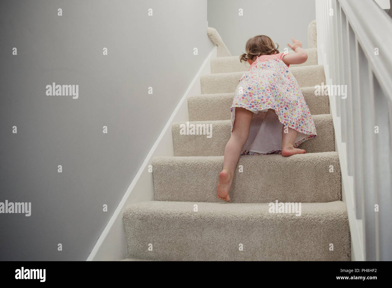Rear view of a little girl climbing up the stairs in the house. She is ...
