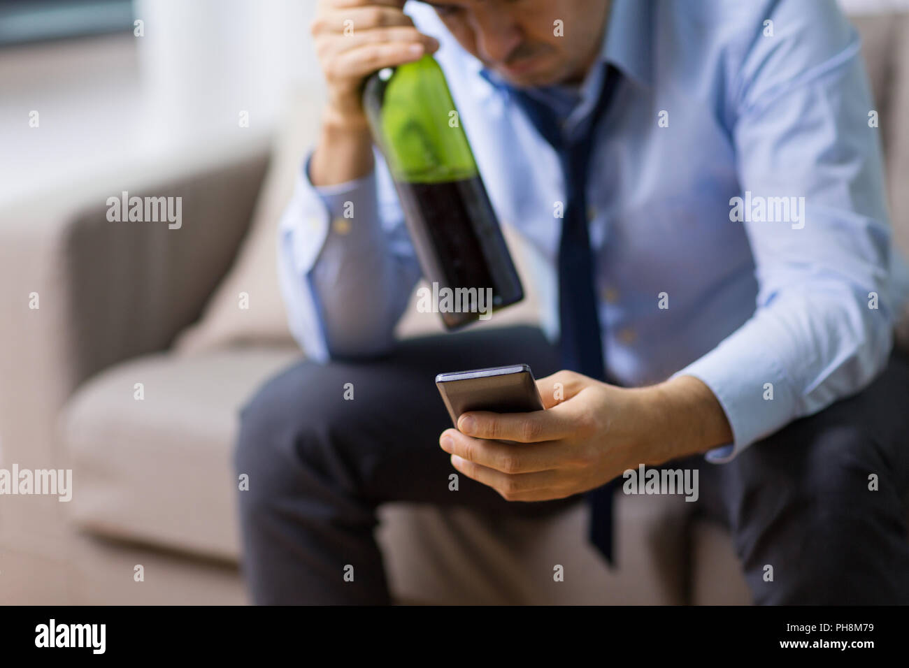 man with smartphone and bottle of alcohol at home Stock Photo