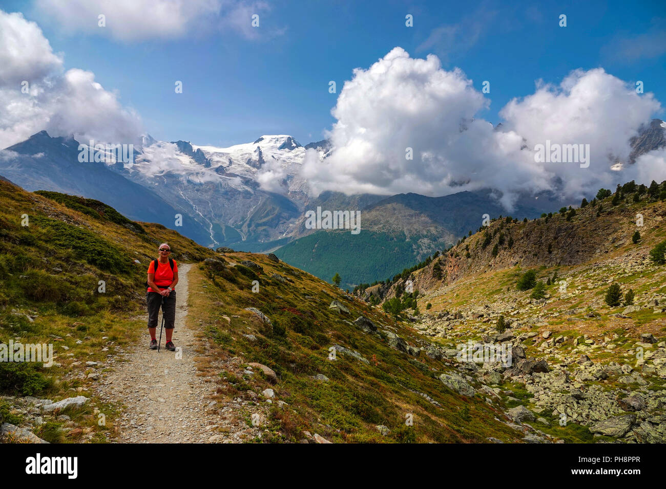 Single female hiker in red, on trail, Summer at Hohe Saas, Hohsaa, cable-car above Saas Grund, Switzerland, Swiss Alps, Stock Photo