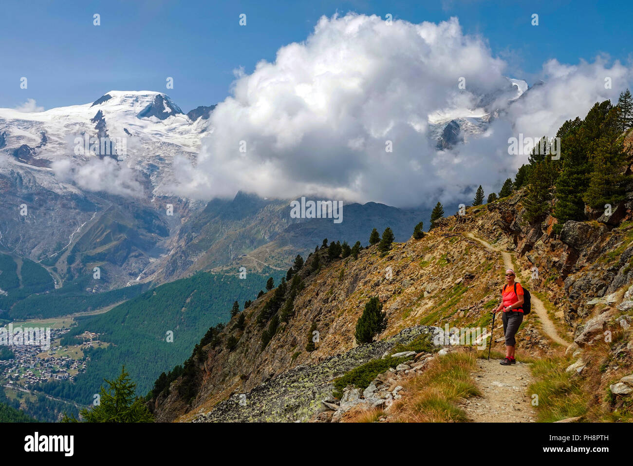 Single female hiker in red, on trail, Summer at Hohe Saas, Hohsaa, cable-car above Saas Grund, Switzerland, Swiss Alps, Stock Photo