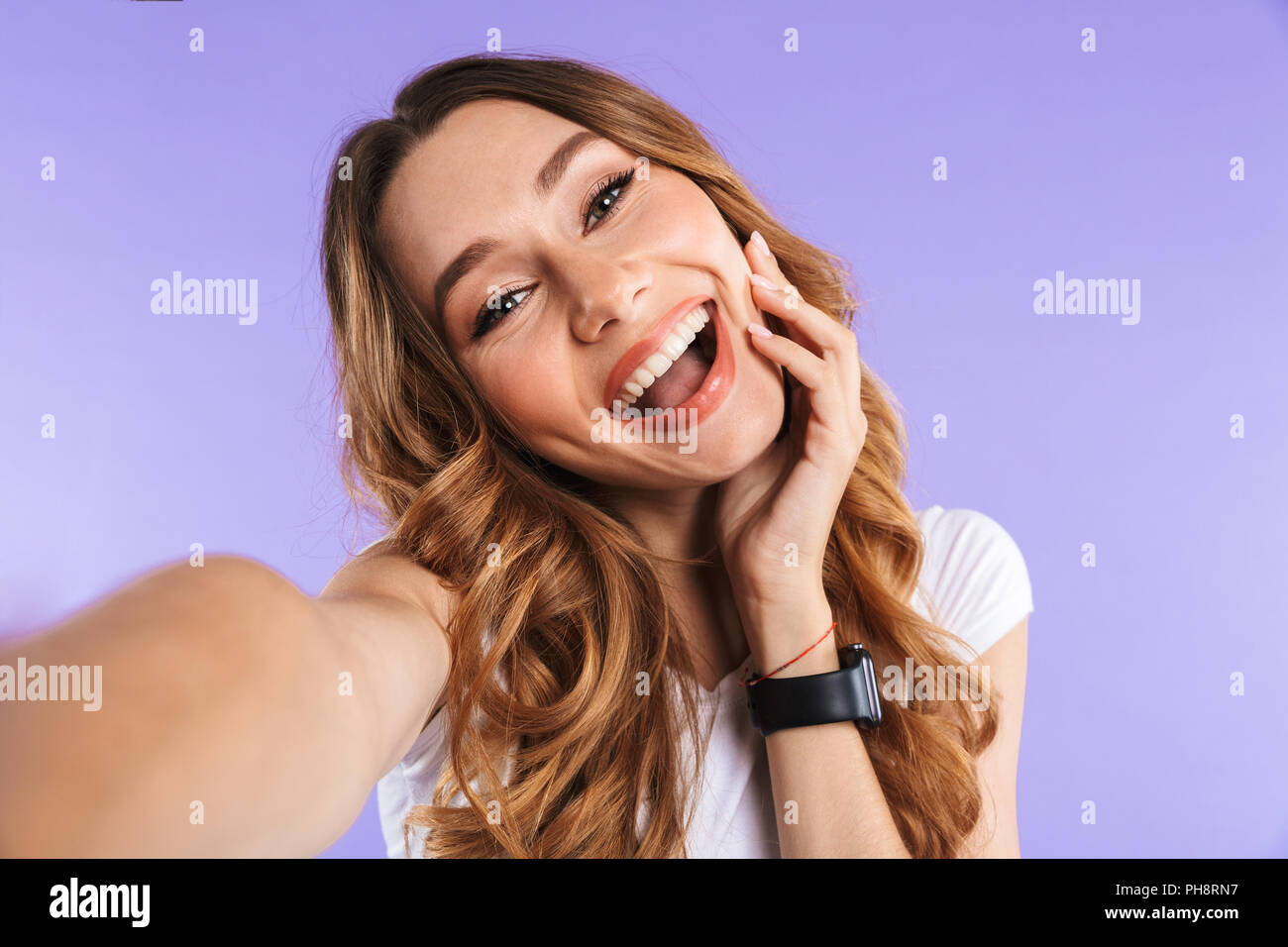 Portrait of a smiling young girl taking a selfie isolated over violet ...