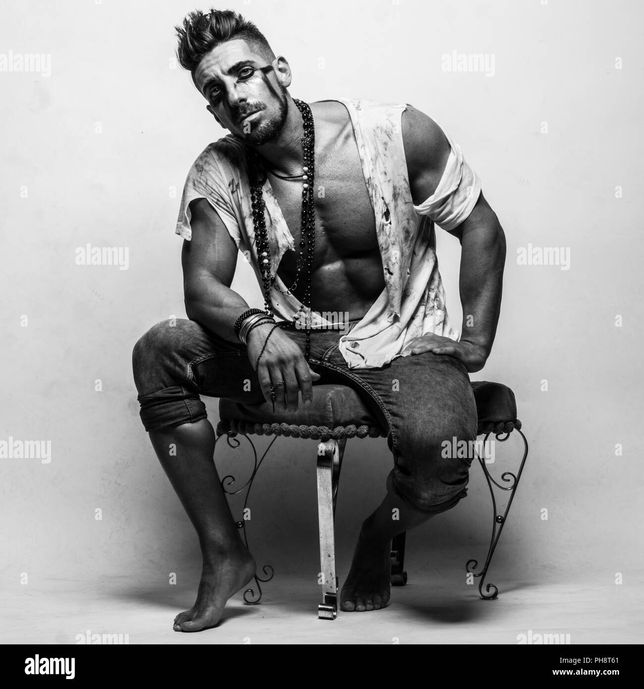 Muscular Man in Ragged Clothes Sitting on a Chair Stock Photo