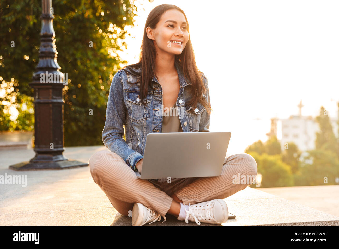 Pretty young asian girl using laptop while sitting on a city street ...