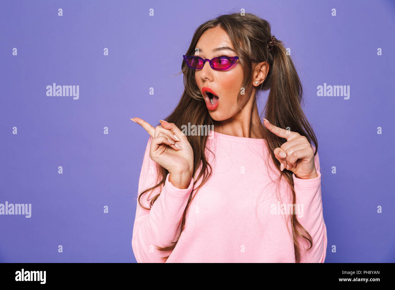 Portrait of a shocked girl in sweatshirt in sunglasses pointing away ...