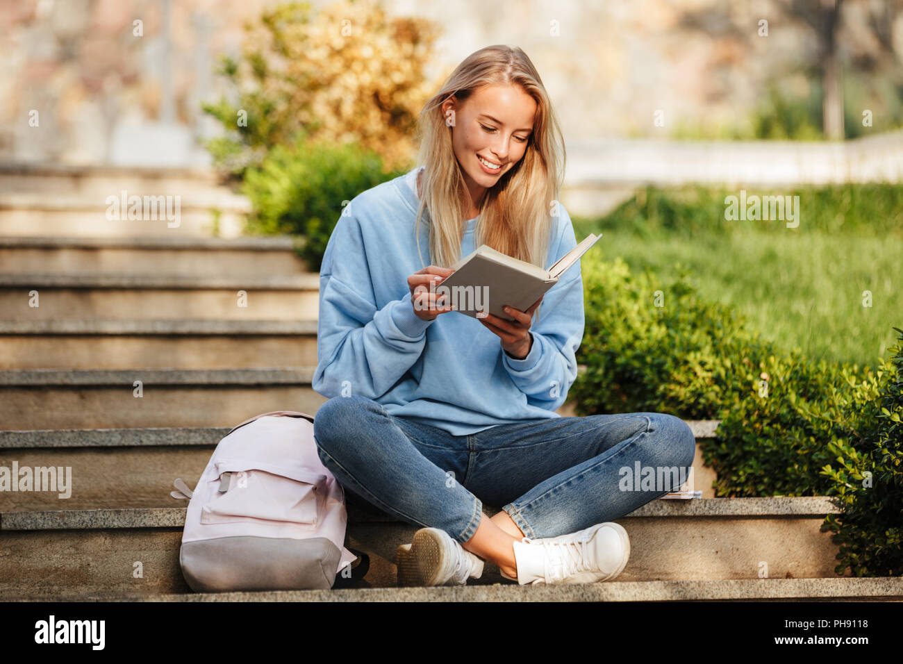 Portrait of a happy young girl student with backpack sitting on steps ...