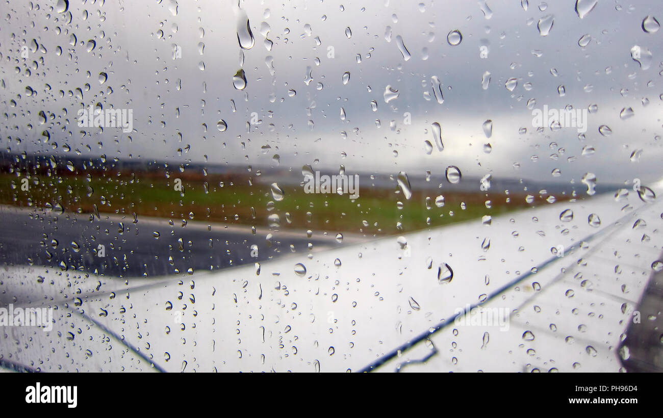 Raindrops on airplane window by the runway. Stock Photo