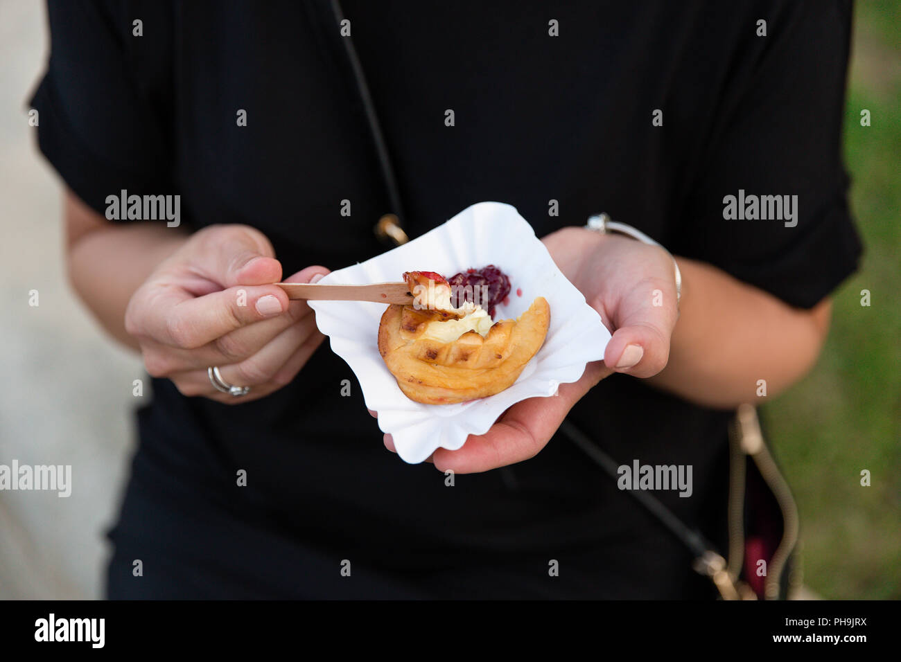Girl eating melted grilled Redykołka Oscypek (a smoked cheese made of salted sheep milk) with cranberry jam on a paper plate in Krosno, Poland Stock Photo