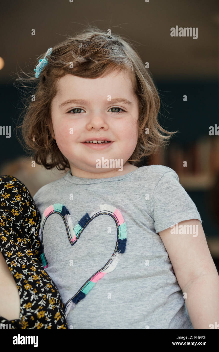 Headshot of a little girl being held by an unrecognisable person for a headshot indoors. Stock Photo