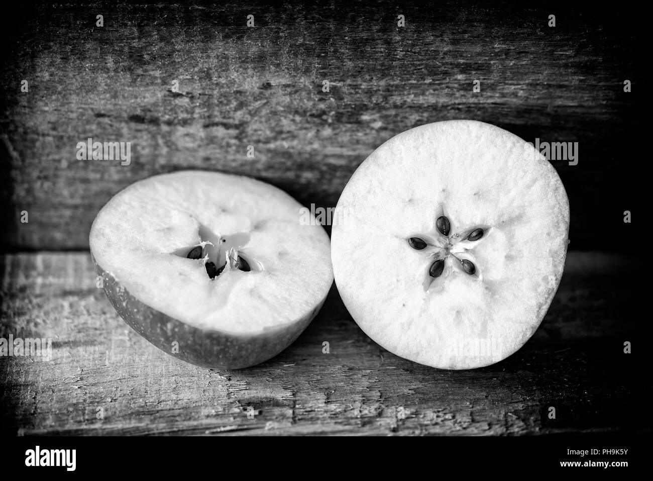 Cut apple on a wooden plank, showing the seeds in a delicate five pointed star motive. Black and white photo Stock Photo
