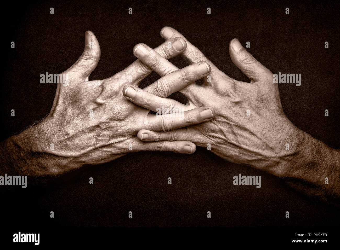 Black and White photo of crossed man's hands with crossed fingers, on dark background, symbolizing protection of security Stock Photo