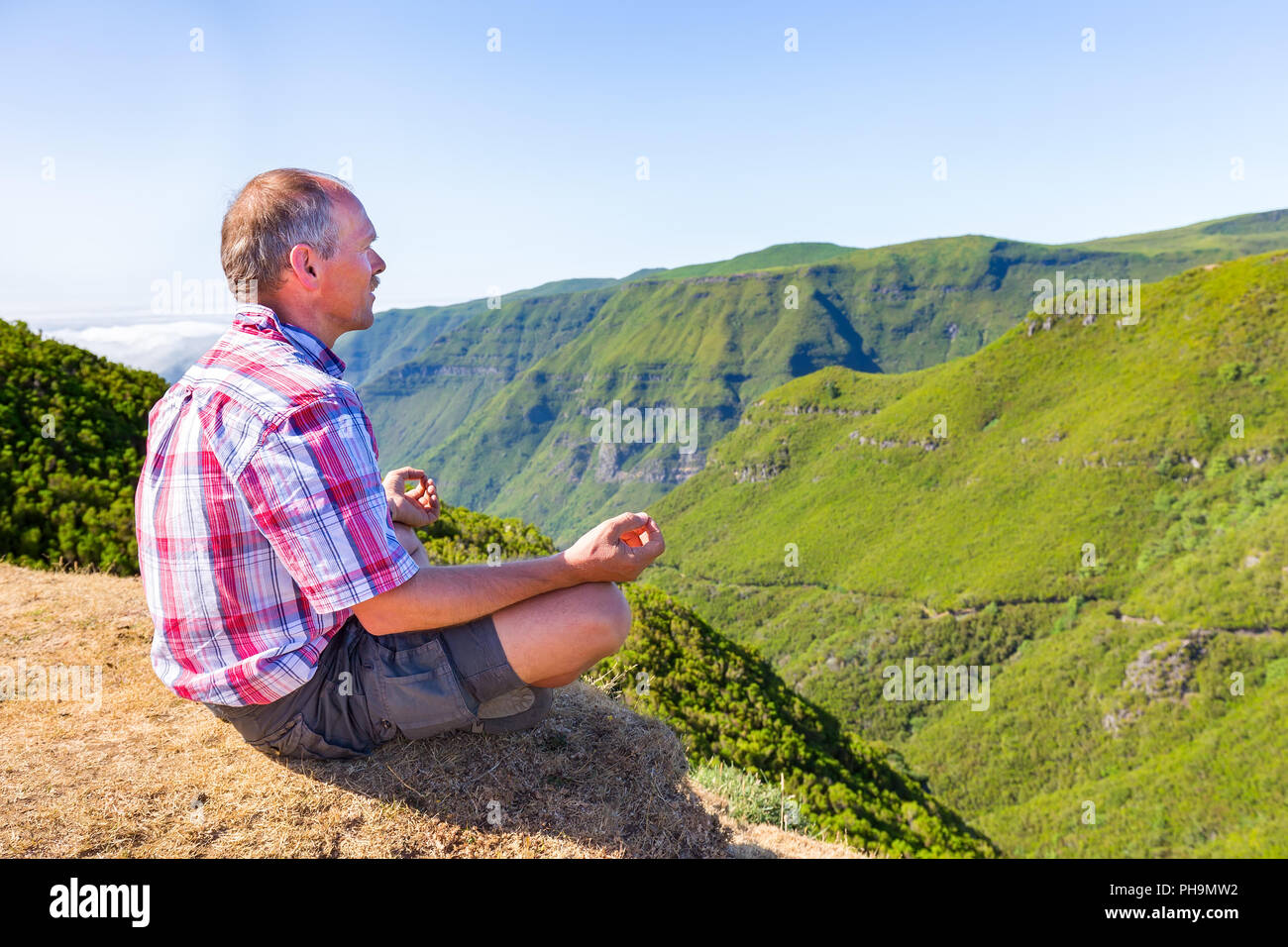 Dutch man meditating on mountain near green valley Stock Photo